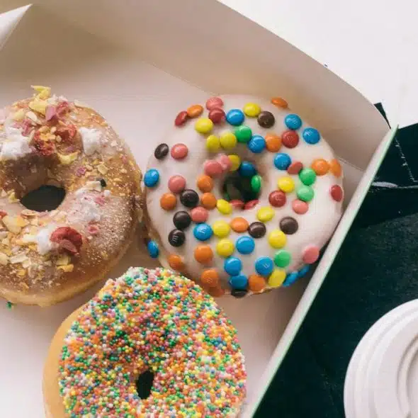 A box with three colorful donuts and a coffee cup.