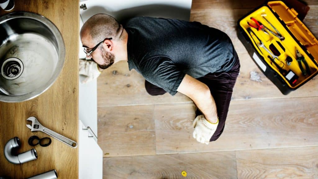 Overhead view of a bald man working under a sink with a toolbox nearby.