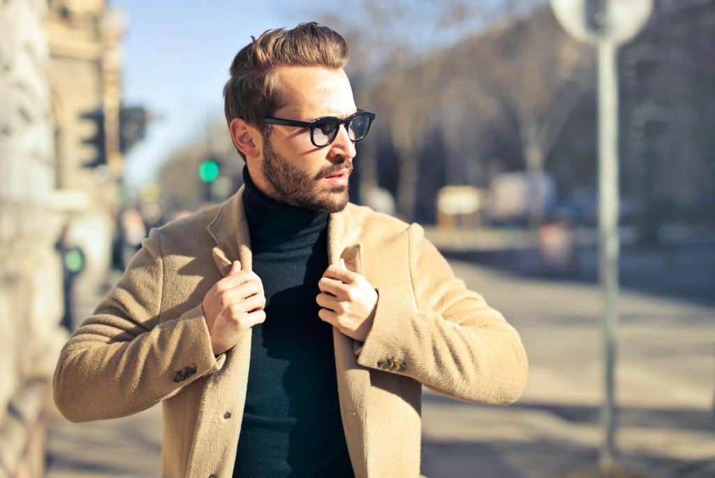 The man is wearing a brown jacket and eyeglasses.