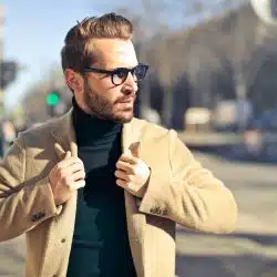 The man is wearing a brown jacket and eyeglasses.
