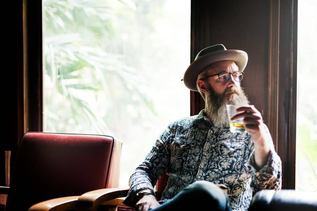 The man is sitting and holding his drink.