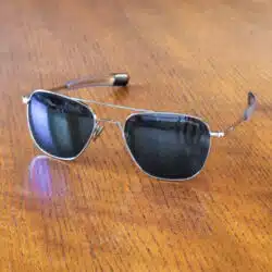 A pair of Randolph Engineering Aviator sunglasses with dark lenses and a silver frame resting on a wooden surface.
