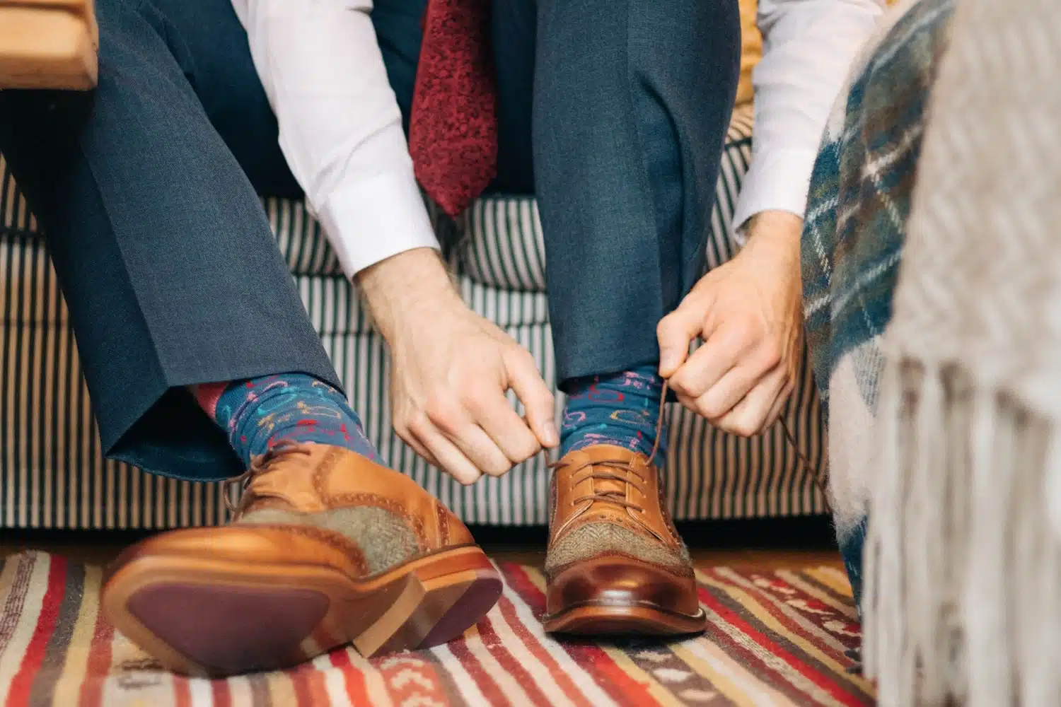 Someone sitting on a couch tying their dress shoe for work.