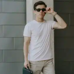 A man wearing sunglasses wearing a light pink t-shirt and khaki pants.