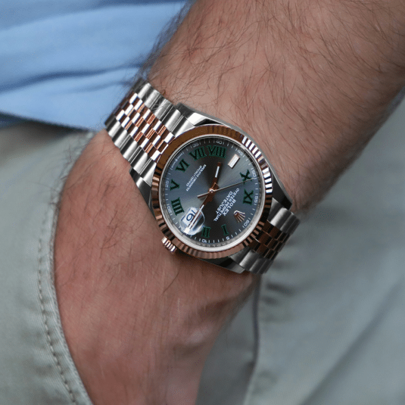 A two-tone Rolex Oyster Perpetual watch with green Roman numerals on a man's wrist.