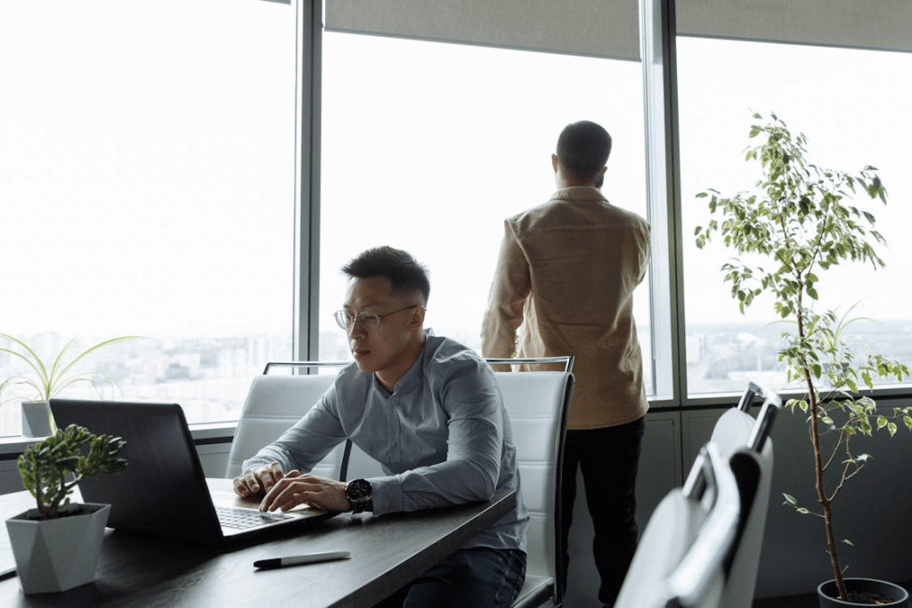 Man in Gray Long Sleeve Shirt Sitting on White Chair while using Laptop